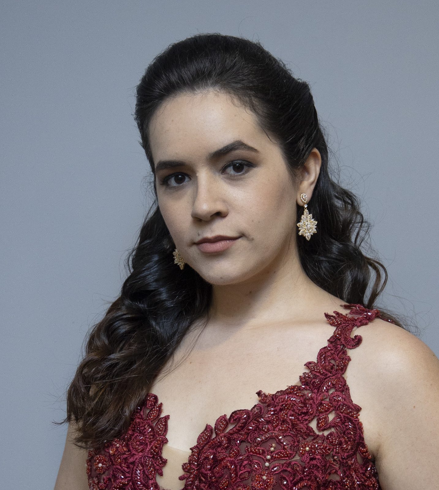 a soprano brasileira Pollyana Santana, cabelos longos presos atrás, com brincos prateados e vestido vermelho